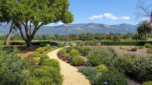 A landscaped garden with a winding path, a large tree, and a view of distant mountains. - Stunning Hope Ranch view home, outstanding amenities, private beach. 30 day min. (Santa Barbara)