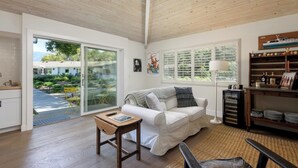 A spacious living room with a white sofa, a wooden coffee table, and a large window offering a view of a garden and neighboring buildings. - Stunning Hope Ranch view home, outstanding amenities, private beach. 30 day min. (Santa Barbara)