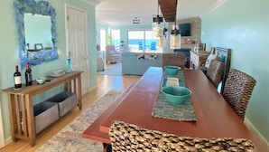A dining area with a long wooden table, benches, and a view of the ocean through large windows.