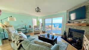 A living room with a sofa, coffee table, and fireplace. There is a large window with a view of the ocean.