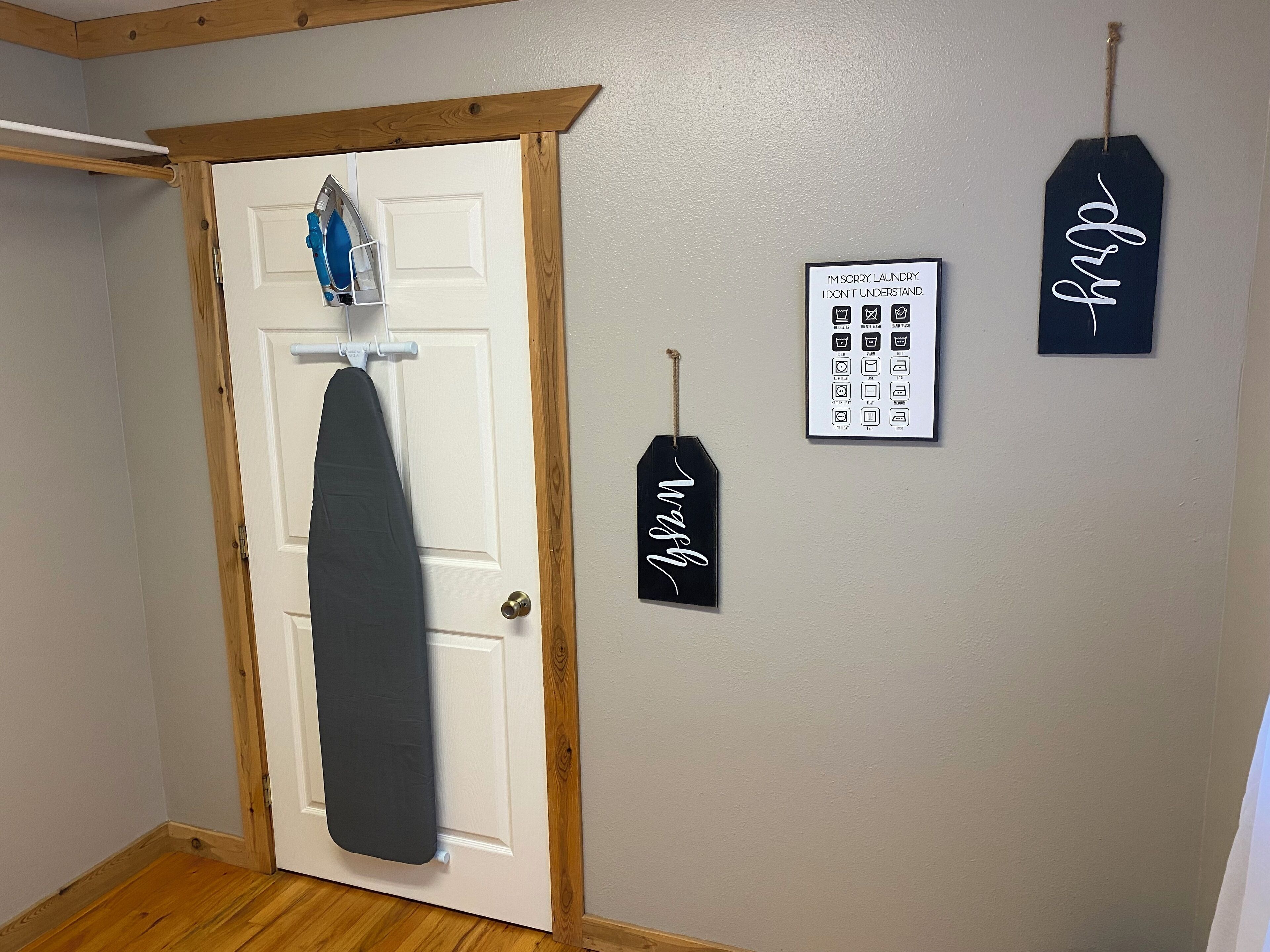 A door with a hanging iron and a towel rack, a framed sign with laundry icons, and a tag with a signature.