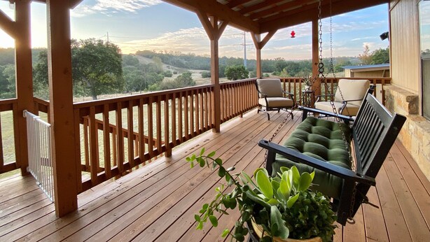 A covered outdoor deck with wooden railings, a bench, and chairs. - A cozy & charming, German-style home in the heart of the Texas Hill Country (Kerrville)