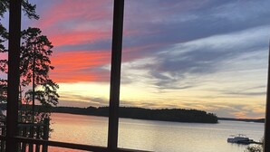 A sunset view from a deck overlooking a calm lake with a boat, surrounded by trees. - Lakehouse on the water with amazing view and private dock
WATER STILL AT DOCK-5' (Clarksville)