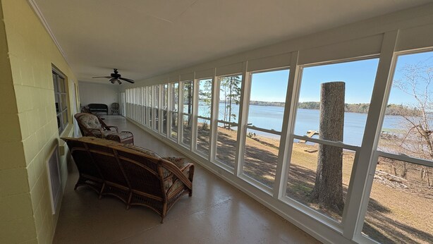 A long room with a view of a lake, wicker furniture, and a ceiling fan. - Lakehouse on the water with amazing view and private dock
WATER STILL AT DOCK-5' (Clarksville)