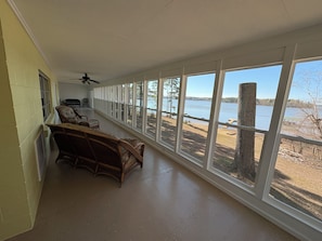 A long room with a view of a lake, wicker furniture, and a ceiling fan.