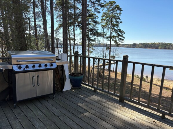 A deck with a grill and a view of a lake.