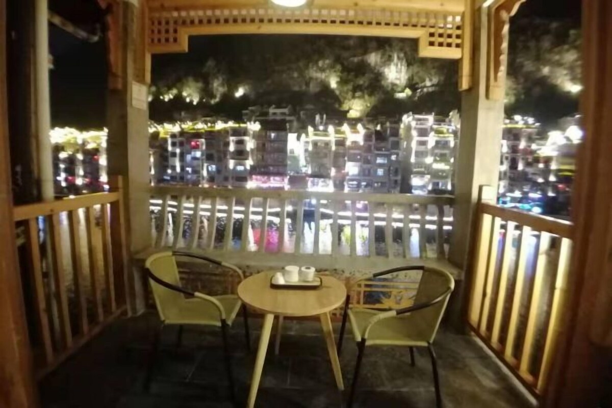 Un balcón con dos sillas y una mesa, con vista a un paisaje urbano de noche.