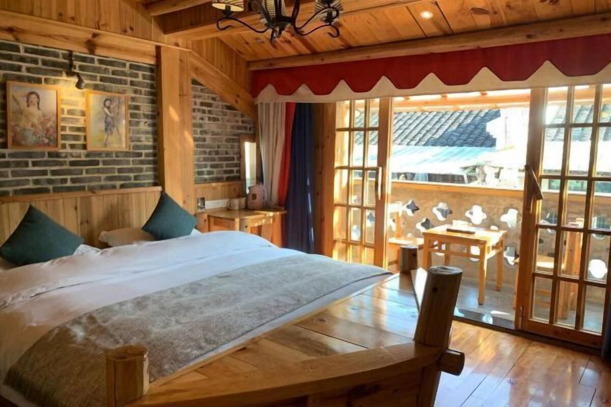 A wooden room with a bed, a table, chairs, and a view through a glass door.