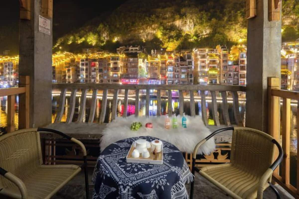 A dining area with wicker chairs, a table with a patterned tablecloth, and a view of illuminated buildings.