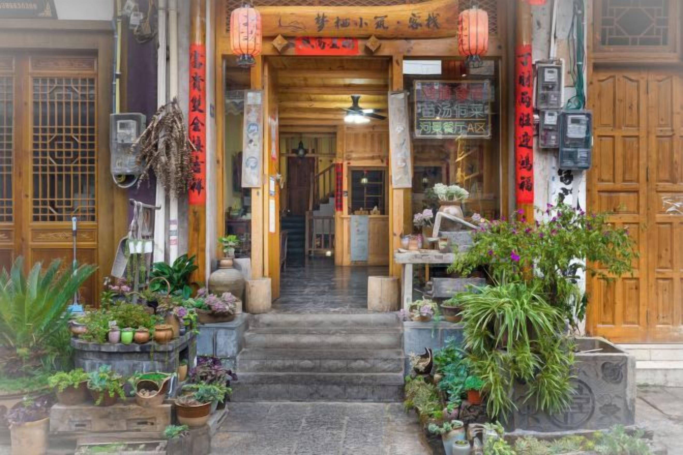 Una entrada tradicional japonesa con puerta de madera, escalones que conducen a la recepción y diversas plantas y decoraciones.