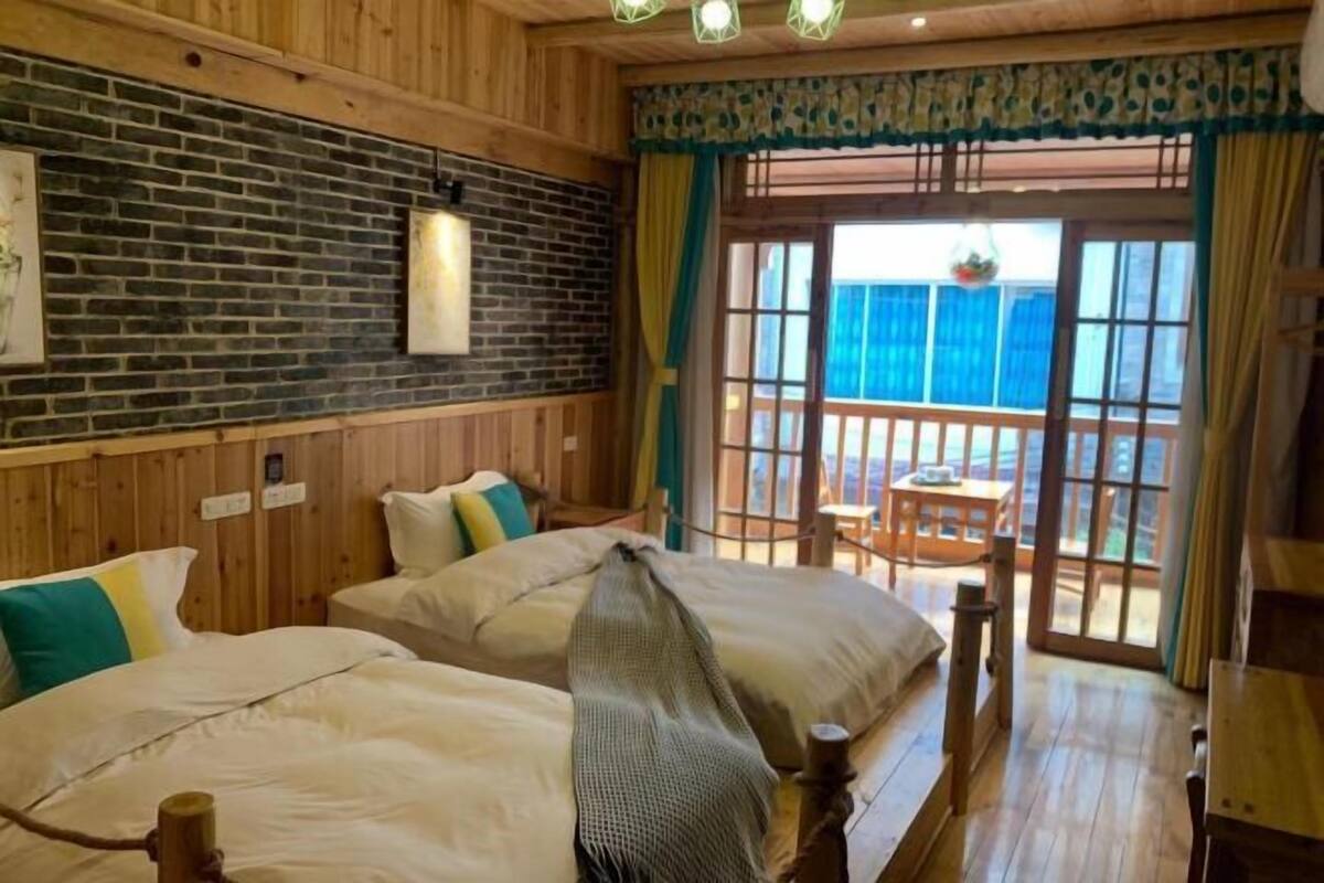 A wooden room with two beds, a brick wall, and a balcony with a table and chairs.