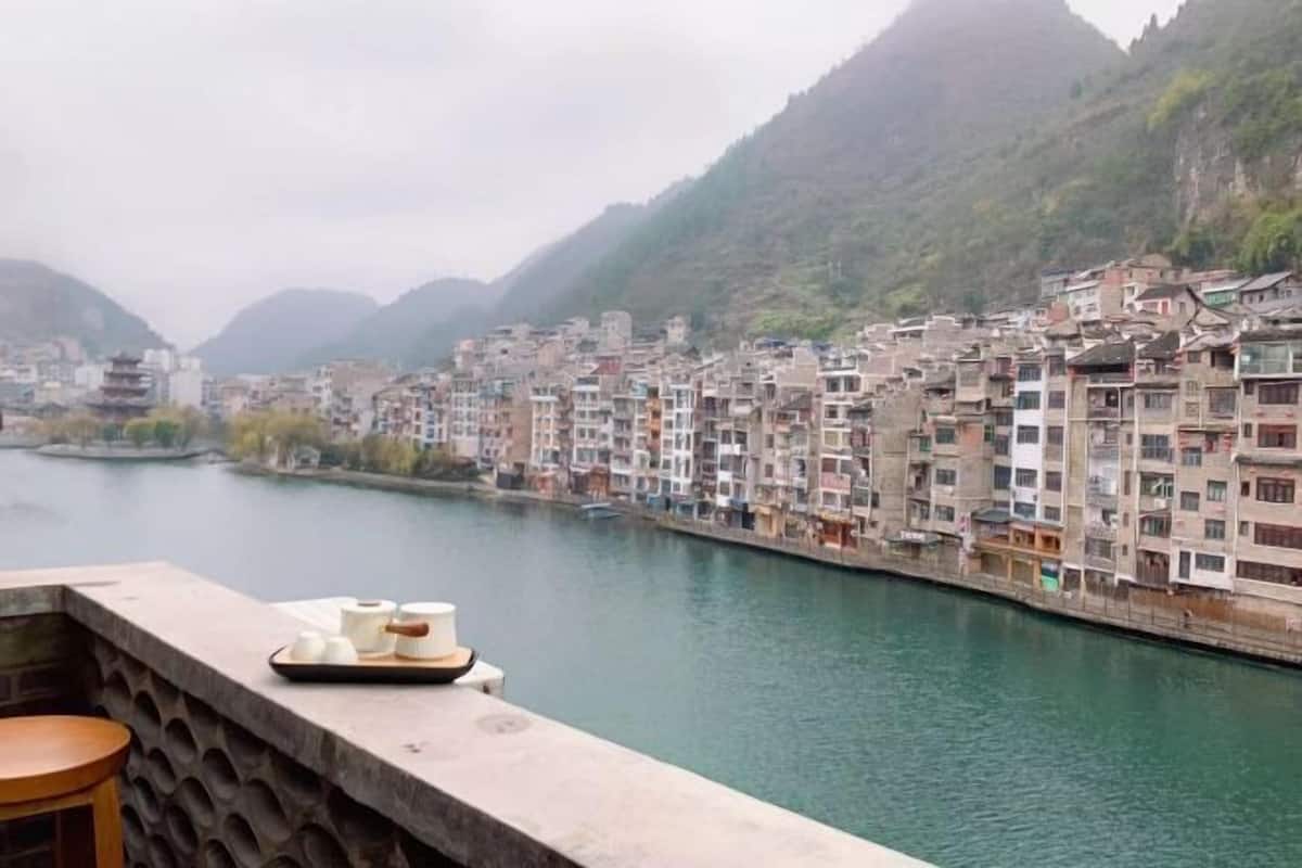 A riverside view of a densely packed residential area with traditional architecture, a wooden bench, and a tray with items on a balcony.