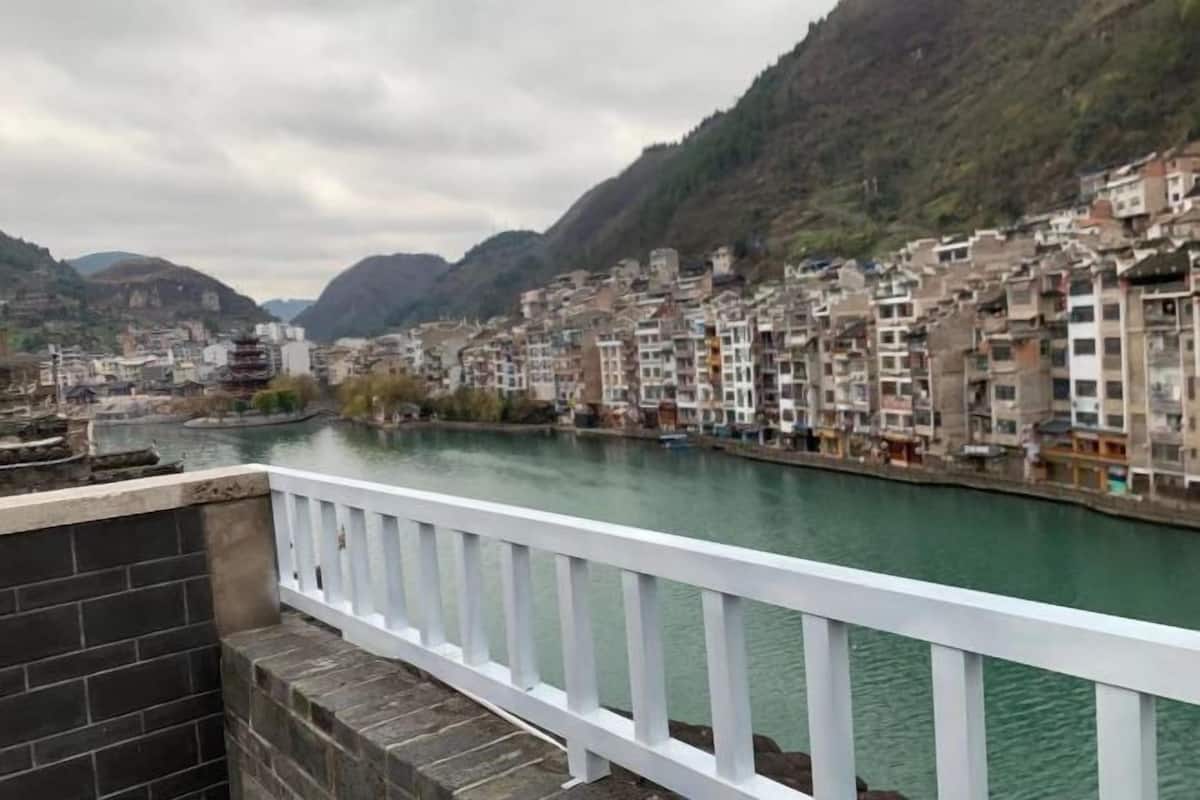 A river with buildings on both sides, a white railing, and a mountainous backdrop.
