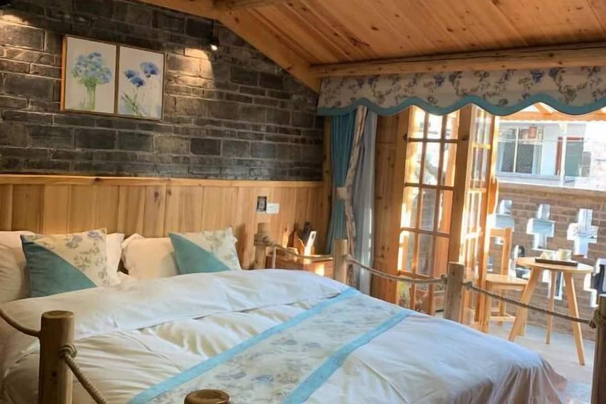 A wooden-framed room with a bed, a brick wall, and a window with curtains.