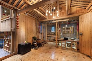 A wooden interior with a high ceiling, a central seating area, and a brick wall with framed pictures.