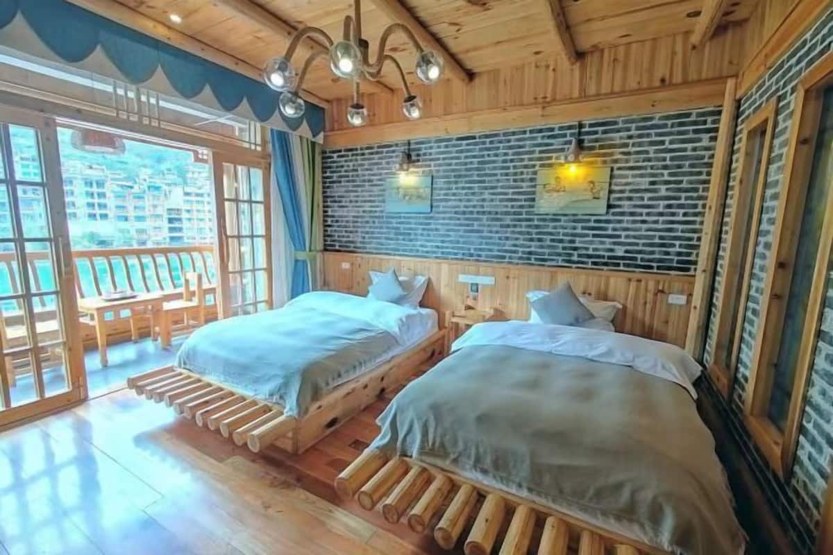 A wooden cabin-style room with two beds, a brick wall, and a balcony with outdoor seating.