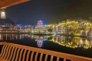 A traditional building with multiple tiers, illuminated by colorful lights, reflecting in a calm body of water. - Mengqi Xiaozhu Inn (Zhenyuan County)