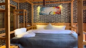 A wooden-framed room with a brick wall, a bed with white bedding, and a colorful painting on the wall. - Mengqi Xiaozhu Inn (Zhenyuan County)