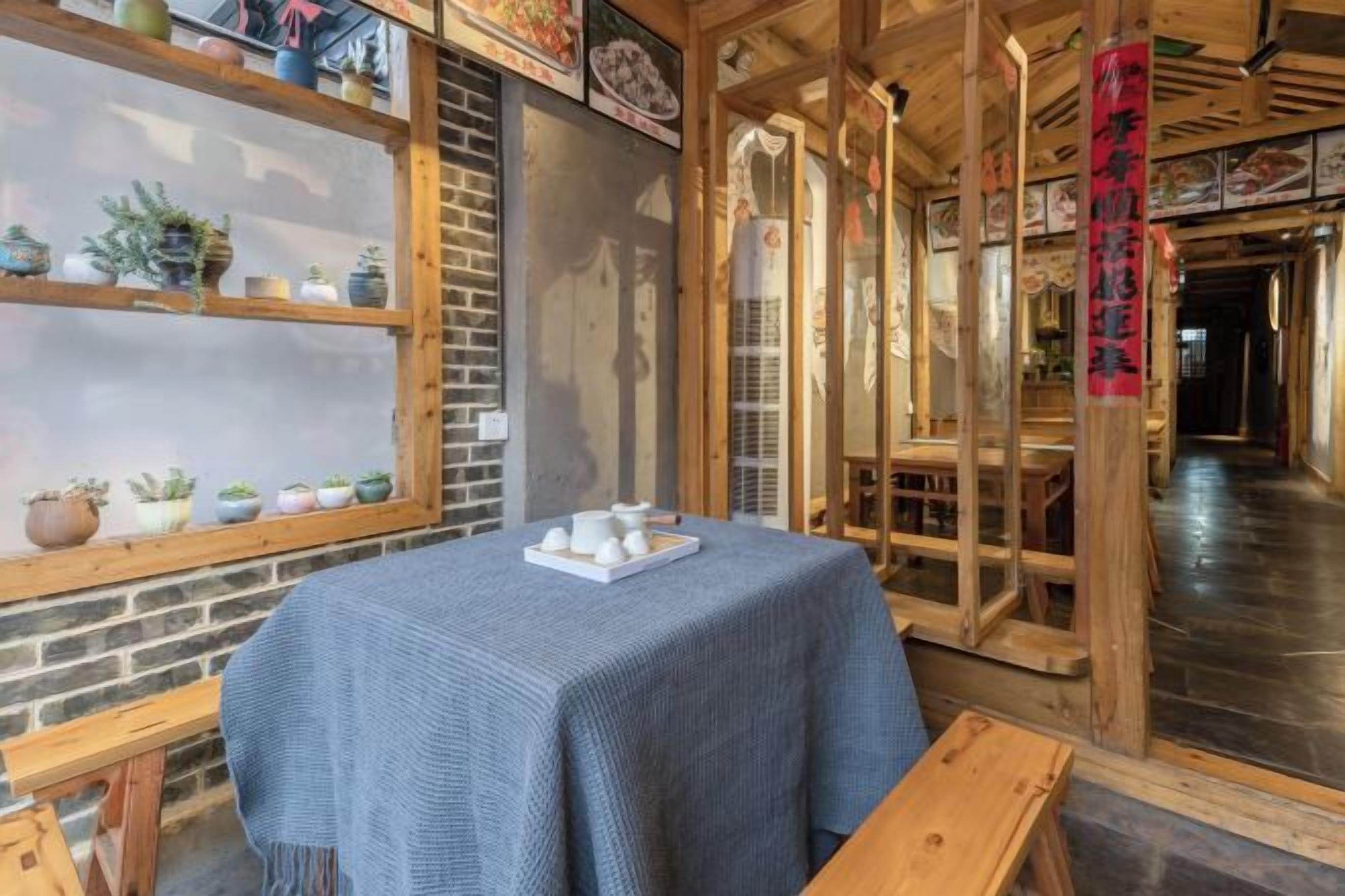 Una habitación con una mesa cubierta con mantel azul, bancos de madera y estanterías con plantas en macetas.