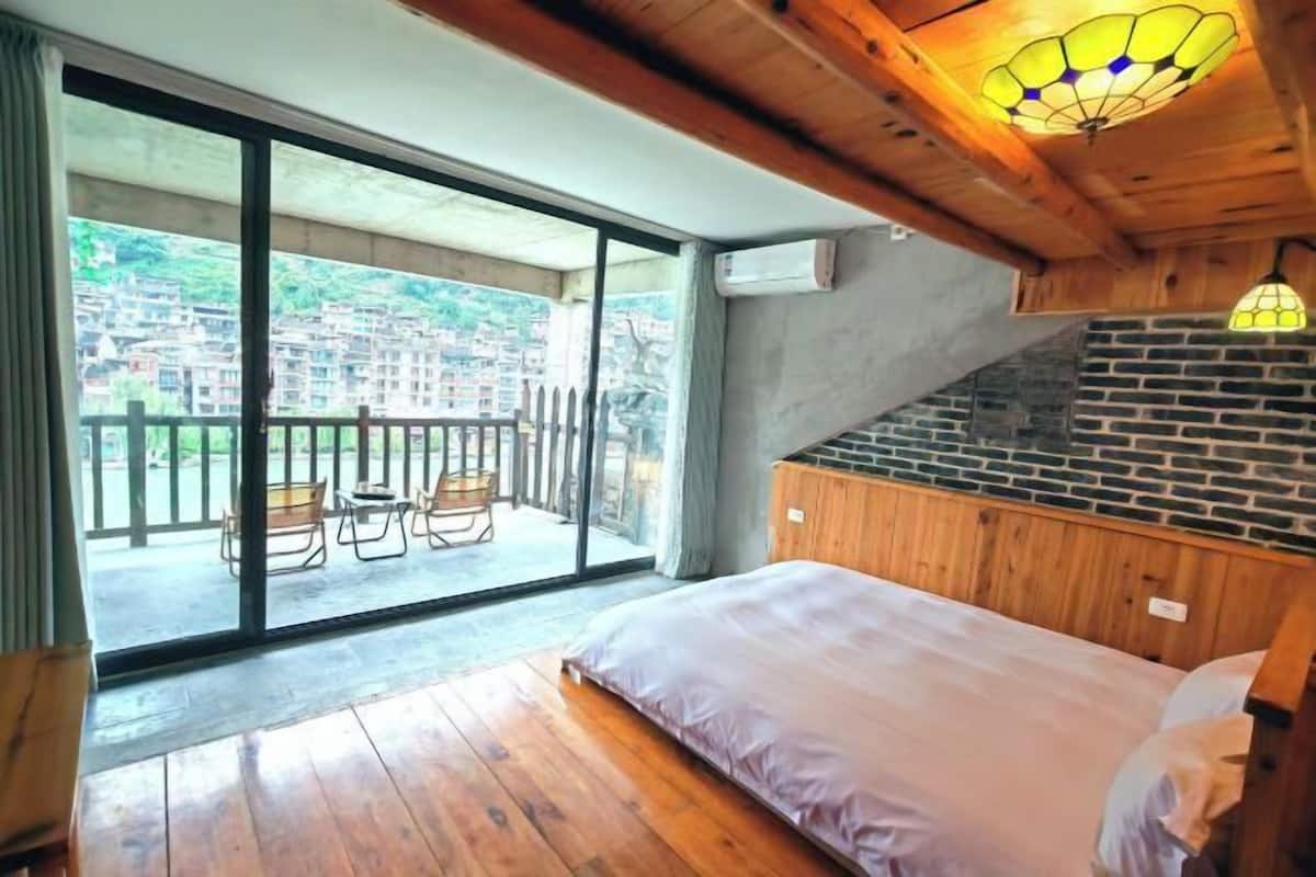 A bedroom with a large bed, a balcony with chairs, and a view of a cityscape.