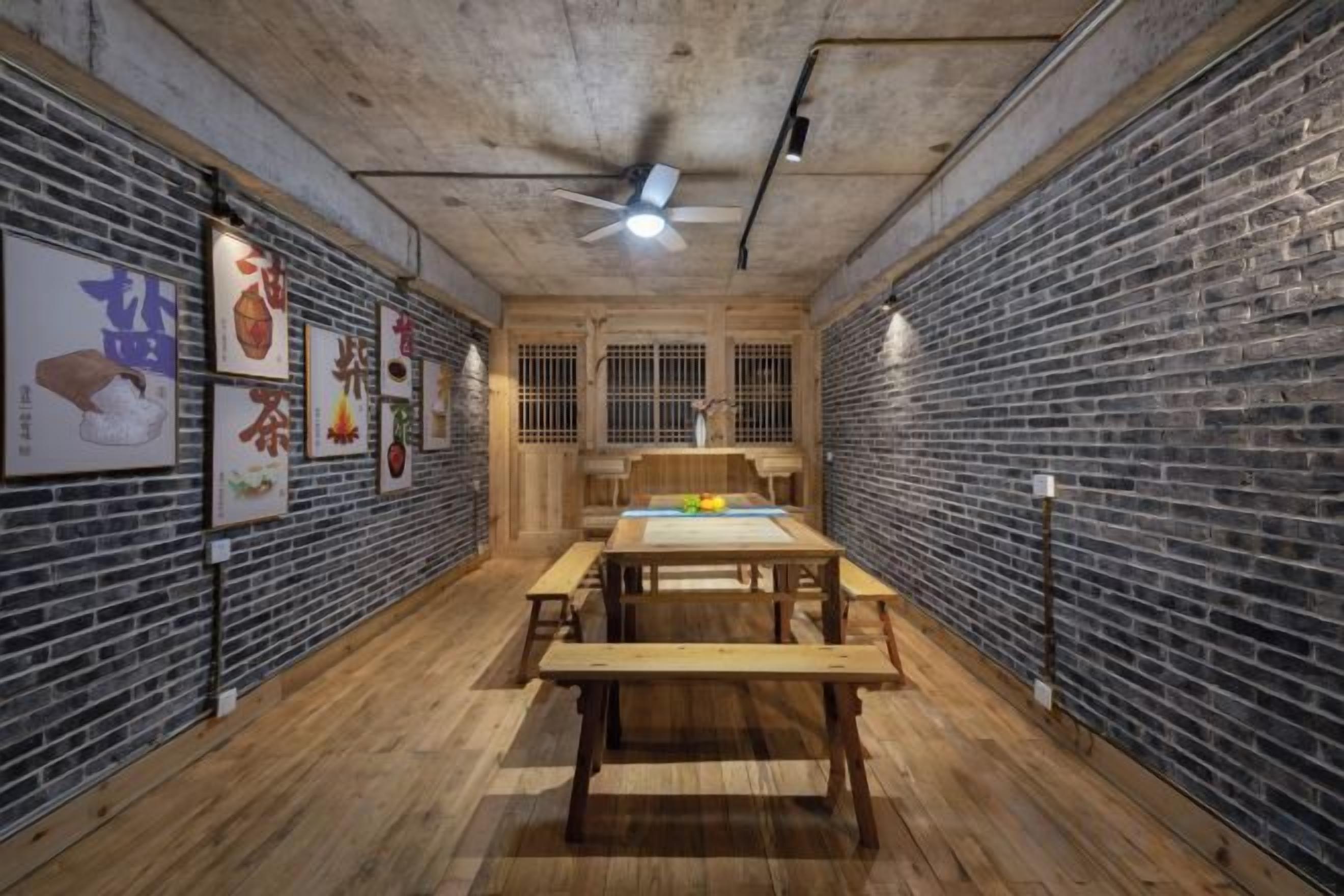 Una habitación con pared de ladrillo, piso de madera, ventilador de techo y una mesa con bancos.