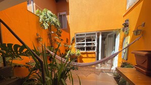 A narrow outdoor space with a hammock, potted plants, and a tiled floor.