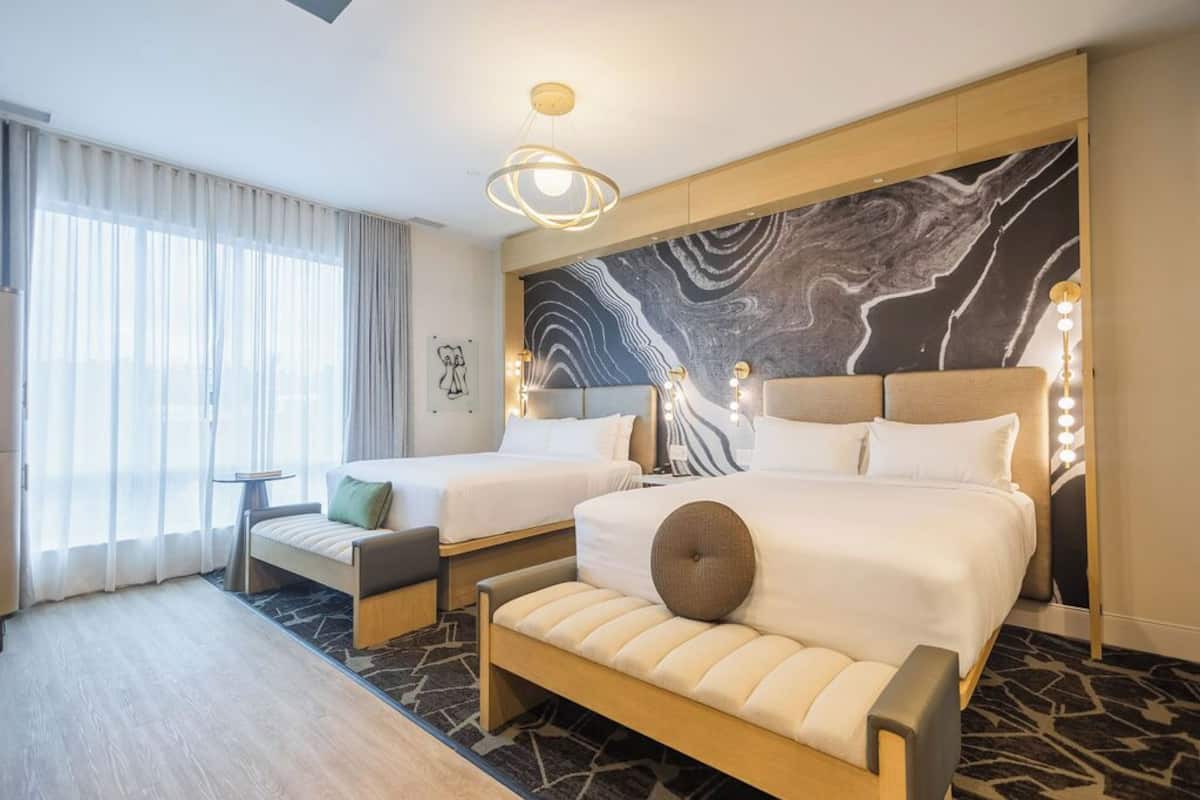 A hotel room with two beds, a sofa, a small table, and a large window with curtains.