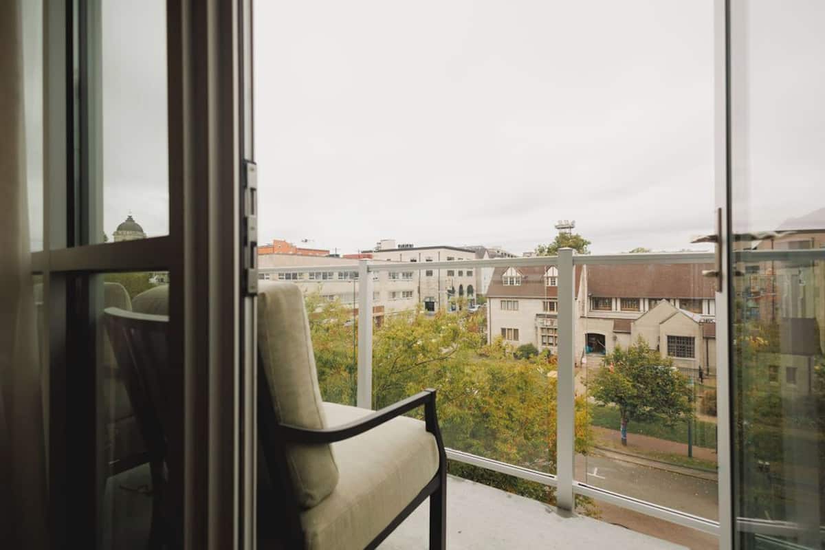 A view from a balcony with a chair, overlooking a residential area with buildings and trees.