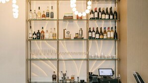 A bar area with a wine and liquor shelf, bar counter, and three bar stools.