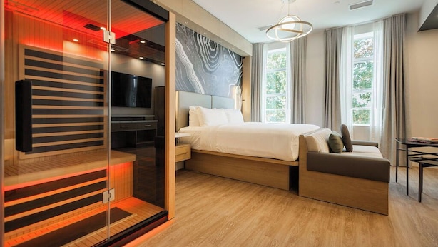 A modern bedroom with a bed, a seating area, a TV, and a large window.
