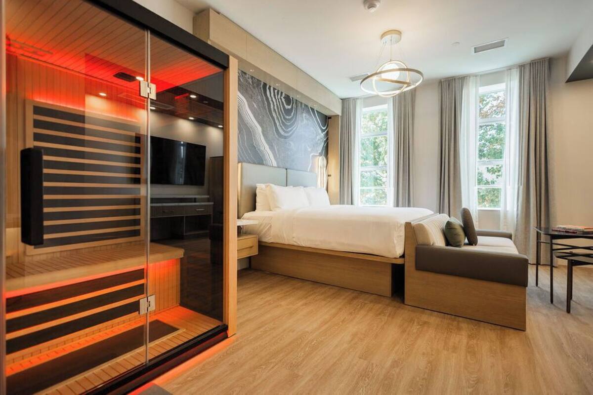A modern bedroom with a bed, a seating area, a TV, and a large window.