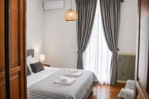 A hotel room with a bed, a bedside lamp, a window with curtains, and a radiator.
