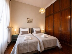 Une chambre d’hôtel avec deux lits, une armoire en bois, un tableau encadré au mur et un luminaire suspendu.
