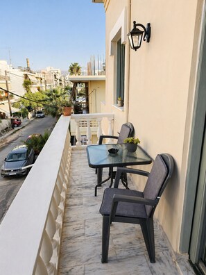Un balcon avec une table et des chaises, un pot de fleurs et, en arrière-plan, une vue sur la rue.
