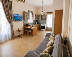 A modern living room with a grey sofa, a small dining table, and a kitchen area with cabinets and appliances.