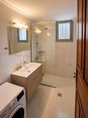 Une salle de bain moderne dotée d’une douche à parois de verre, d’un lavabo avec un meuble-vasque en bois et d’un lave-linge Bosch.