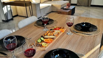 A dining table set with plates, glasses, and a charcuterie board in a modern living room with a sofa and a lamp.