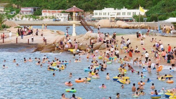 Une plage bondée où l’on voit des gens se baigner et utiliser des bouées gonflables.