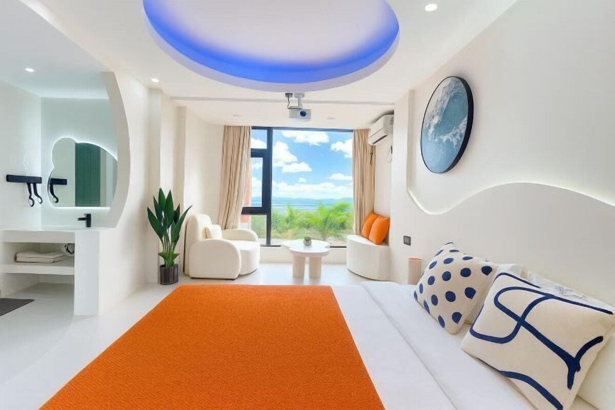 A modern hotel room with a large bed, a sofa, a coffee table, and a view of the outdoors.
