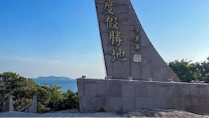 Un monument orné d’inscriptions, se dressant sur fond de ciel dégagé et offrant une vue lointaine sur la mer.