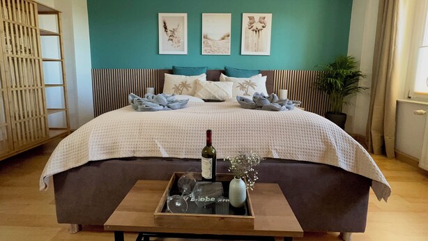 Un dormitorio con cama, una mesita de noche con una botella y un vaso, y una bandeja con un florero.