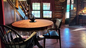 A rustic wooden interior with a round wooden table, chairs, a lamp, and a window with a view of greenery. - Vintage Log Cabin in the Heart of the Adirondacks (Indian Lake)