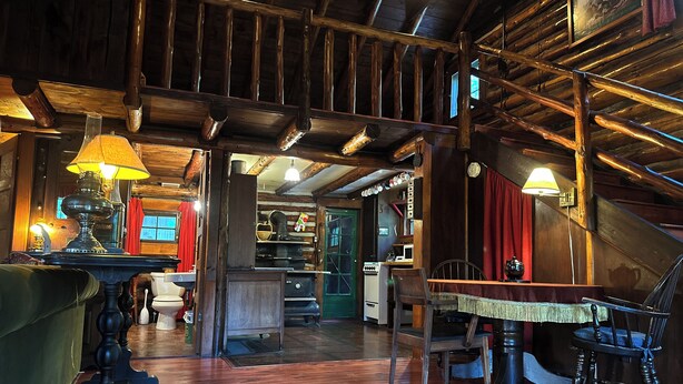 A rustic wooden interior with a dining area, kitchen, and a staircase leading to an upper level. - Vintage Log Cabin in the Heart of the Adirondacks (Indian Lake)