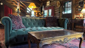 A log cabin interior with a tufted teal sofa, a wooden coffee table, and a rustic ambiance. - Vintage Log Cabin in the Heart of the Adirondacks (Indian Lake)