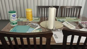 A dining table with a paper towel holder, a bottle of disinfecting wipes, and some magazines.