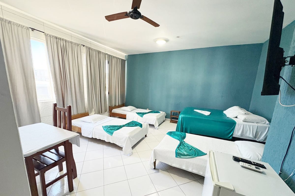 Habitación de hotel con dos camas individuales, un escritorio, una silla, un ventilador de techo y una ventana con cortinas.