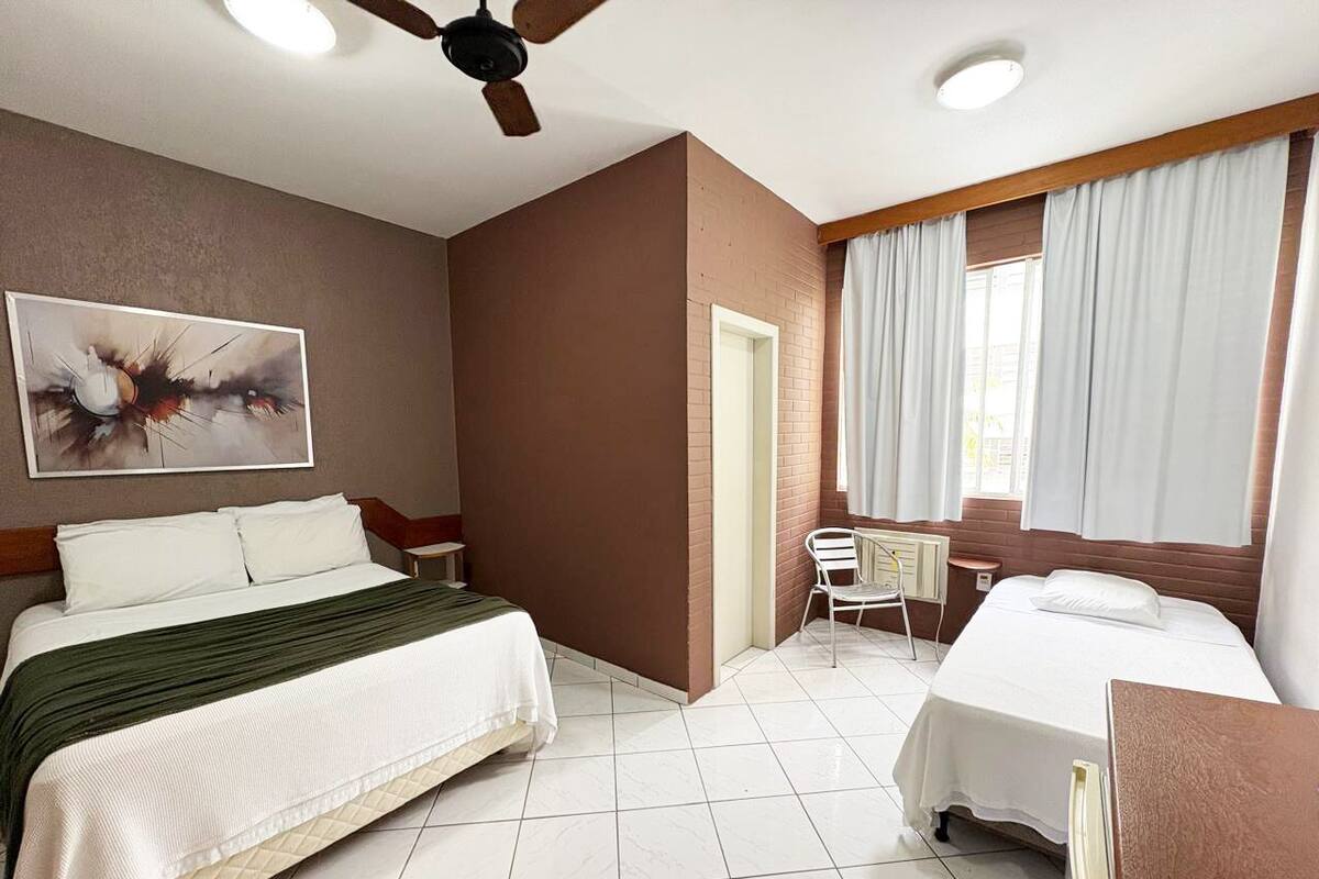 Una habitación de hotel con una cama, un escritorio, una silla, un ventilador de techo y un cuadro en la pared.