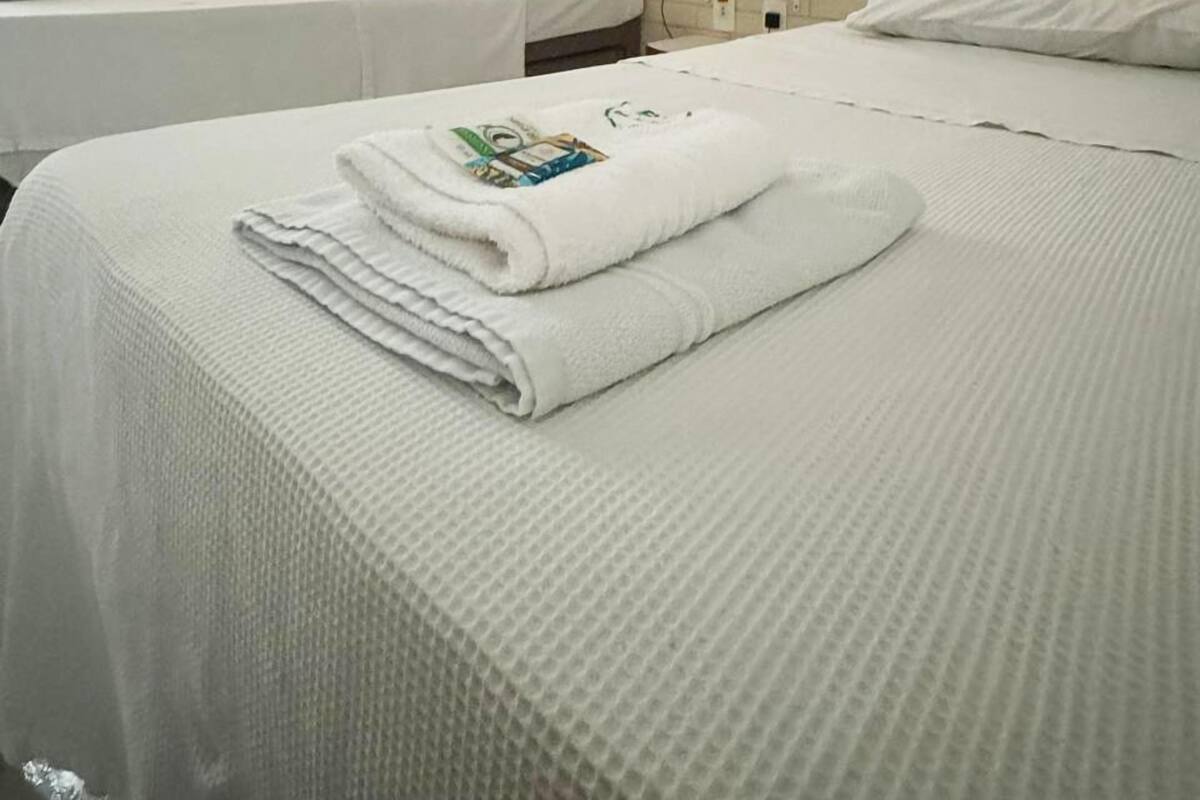 Habitación de hotel con dos camas, una pared de ladrillo, una ventana con cortinas y una mesita de noche.