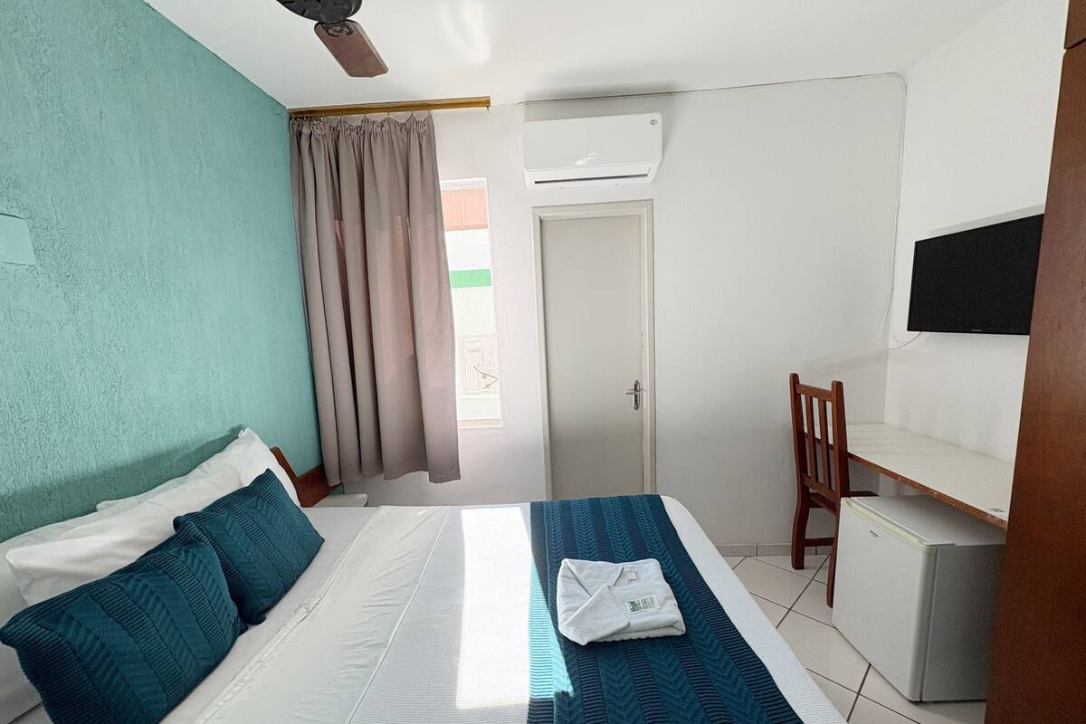 Un dormitorio con cama, escritorio, silla, aire acondicionado y televisor.