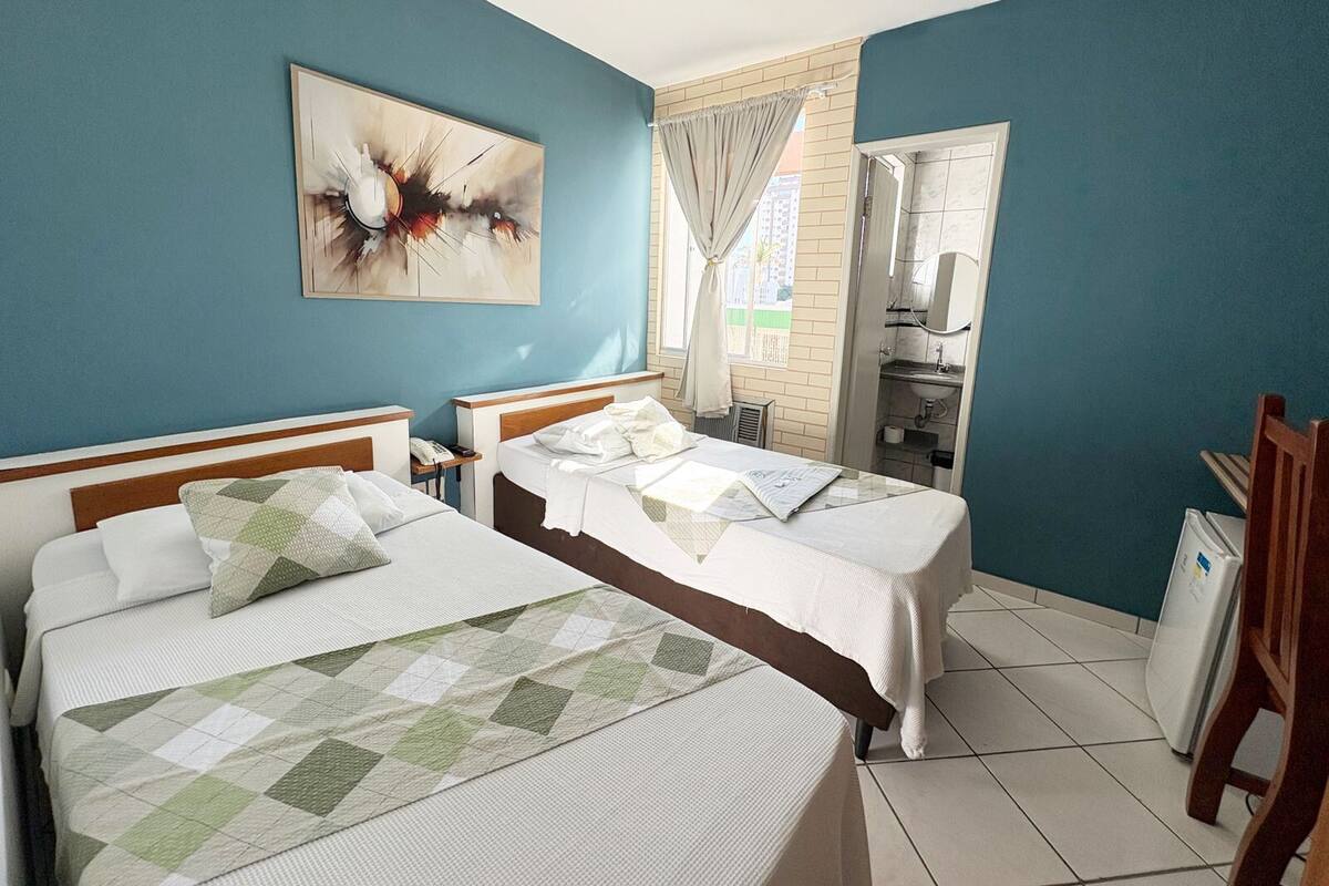 Habitación de hotel con dos camas, baño y un amplio ventanal con cortinas.